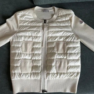 Moncler cardigan - Säljer en vit Moncler cardigan i storlek i M i en kräm vit färg. NY PRIS 8600. Använd bara ett få tal gånger då jag använt andra jackor istället. Skick är 9/10 med inga fläckar eller märken. Skriv för fler bilder eller eventuella frågor.