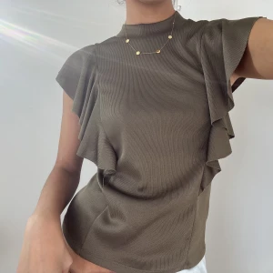 Grön tröja - Kakigrön/olivgrön tröja med fina volanger på axlarna. En absolut favorit i garderoben som funkar till alla tillfällen! Passar XS-M (ser mer brun ut på bilderna men är grön!)