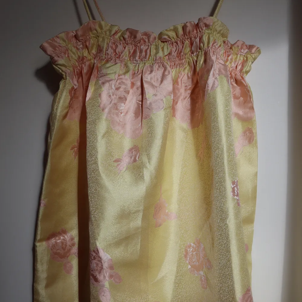 Gul klänning med rosa blommor. Köpt i Danmark, helt oanvänd, perfekt skick! Prislappen är fortfarande på, köpte för att ha på ett bröllop men blev en annan klänning så därför säljer jag den 💐. Klänningar.