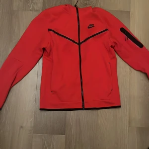 Nike tech - Säljer min röda väldigt fina Nike tech som inte kommer till användning. Ny pris är runt 1300/1400. Köptes på Nikes egna hemsida i början av året och priset kan diskuteras. Har en pytteliten fläck som inte syns framifrån och ej testat tagit bort.