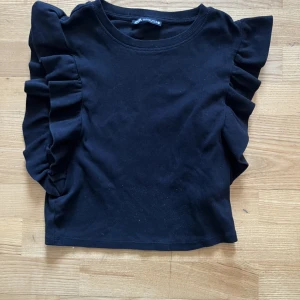 Svart topp från Zara i small - Svart topp från Zara med volang vid ärmarna i storlek small. Använd ett fåtal gånger.