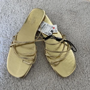 Guldiga sandaler/tofflor Zara - Ett par oanvända guldiga sandaler från Zara. Helt oanvända i strl 39. 