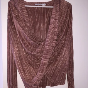 Omlott blus - Skimrig omlottsblus från NA-KD, roseguld/lila