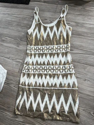 Klänning Mini - Paljettklänning med fint mönster. Vit och guld.