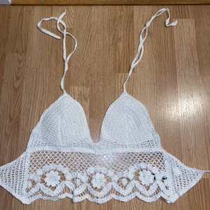 Vit/ljus beige virkad topp - Fin virkad topp, perfekt till sommaren. Ett av snörena är lite trasigt men det märks inte när man har knutit den (se bild 3). Annars bra skick och inte använd allt för många gånger. Svårt att säga exakt storlek men den går att justera.