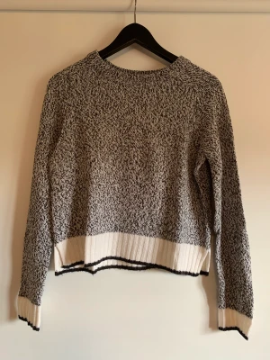 Stickad tröja - Grå stickad tröja från HM med en vit och svart rand på ärmar och på slutet av tröjan. Storlek XS. Använd en del men inget synligt slitage och tvättad sparsamt. 