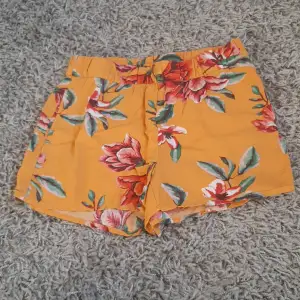 Ett par blommiga orangea barn shorts. Original pris är 249kr.
