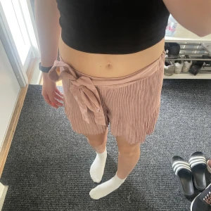 Shorts/Kjol - Söta shorts som, när de sitter på, ser ut som en kjol. Materialet är lite ribbat och ganska tunt. Två stycken band som man knyter till en rosett på ena sidan. 
