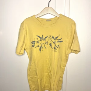Gul T-shirt med tryck - En gul somrig T-shirt med tryck av blomma på från Urban outfitters. Tröjan är i bra skick och är endast använd fåtal gånger🤍Storleken är M men skulle säga att den passar alla som är XS - M