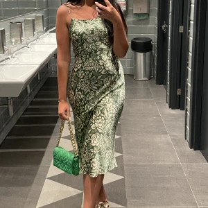 Mönstrad satinklänning  - Mönstrad satinklänning från Zara. Den är grön och har vita blommor som mönster. Har bara burit den en gång och har sen dess inte funnit tillfälle att bära den. Har också växt ifrån denna stil, så därför är den till salu. Den är normal i storlek (M).