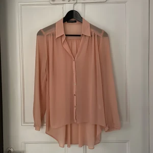 Atmosphere blus rosa  - Strl. 38. Meshblus rosa. Lång genomskinlig med pärlemor liknande knappar. 