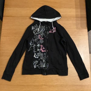 Svart Y2K Zip-Up - Galet snygg zip-up från Cellbes Vita och rosa floral-pattern och fjärilar längs framsidan. 42/44 Känns som en stor M! Finns tecken av användning men ej slitage! Skriv om det finns några frågor :)