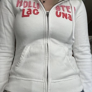 hollister huvtröja  - en vit huvtröja från hollister med rosa text🥰