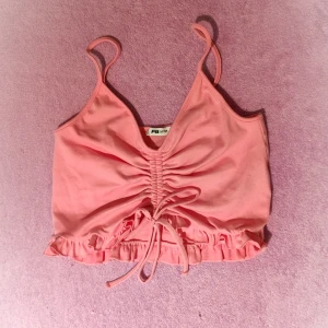 Rosa sommartopp - Kort rosa rosettformad topp med volangiga axelband.  Ny och oanvänd.  Materialet är flexibelt och mjukt vid beröring.