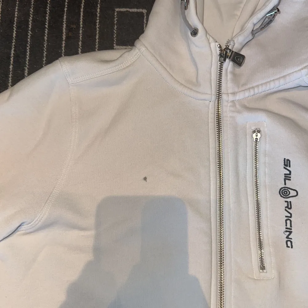 En vit väldigt bekväm Sail Racing hoodie. Väldigt bra skick förutom en svart prick (se bild 3). Säljer då jag har bytt stil och original värde 1300, säljer för 550!. Tröjor & Koftor.