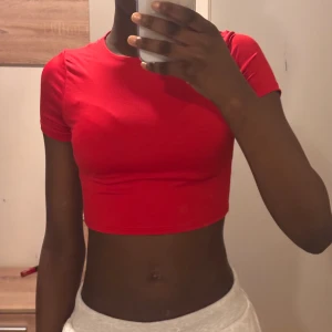 Röd croppad topp med kort ärm - Säljer en röd croppad topp med rund hals och korta ärmar. Toppens tighta passform framhäver midjan och den är tillverkad i mjukt och stretchigt material, troligen bomull eller polyester. Perfekt för dig som gillar färgstarka och enkla plagg.