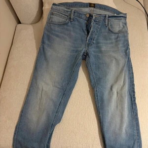 Lee Daren Button ljusblå jeans W33 L32 - Säljer ett par Lee Daren Button jeans i ljusblå tvätt med klassisk femficksdesign och knappgylf. Jeansen har raka ben och normal passform, tillverkade i mjukt bomullsmaterial. Perfekt för dig som gillar en avslappnad och stilren look.
