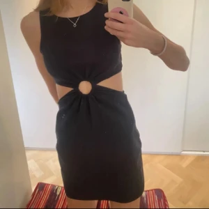 Zara klänning - Snygg svart kortklänning med cut-out i midjan och en cool ringdetalj framtill. Ärmlös modell med tight passform och högt skuren hals. Perfekt för dig som vill sticka ut med en trendig look. Passar S-M