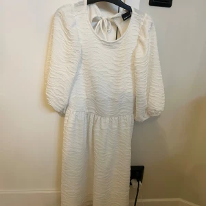 Vit omlottklänning med puffärm - Superfin vit klänning från Gina Tricot med strukturmönster, puffiga trekvartsärmar och snygg öppen rygg med knytband. Använd en gång.
