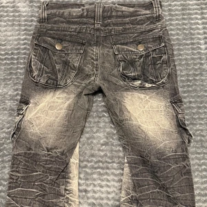 Grå cargopants från TopIsm - Säljer ett par grå cargopants från TopIsm med coolt slitna detaljer och kontrastfärgade partier. Byxorna har flera stora fickor med tryckknappar och en loose passform. Materialet är jeans och de har en unik, skrynklig look som sticker ut. Säljer då dom är för små för mig.