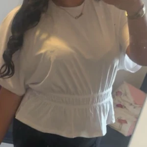 Vit blus med resår i midjan - Säljer en söt vit blus med korta ärmar och resår i midjan som ger en snygg form. Blusen har en luftig passform och är perfekt för dig som gillar en enkel men stilren look.