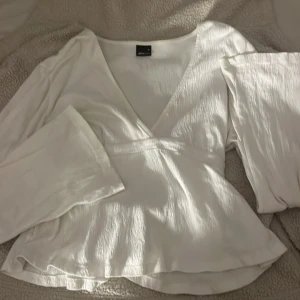 knytblus - Säljer en vit omlottblus från Gina Tricot med v-ringning och långa vida ärmar. Blusen har knytband i midjan och är tillverkad i ett lätt, glansigt tyg med lite struktur. Perfekt för dig som gillar en feminin och trendig look.