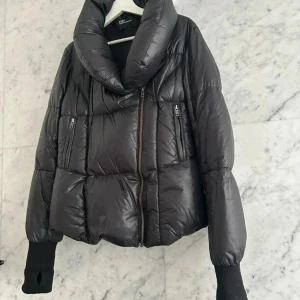 Svart dunjacka med stor krage M/L - Pufferjacka: fluffig varm svart dunjacka med fluffig krage och långa muddar från designermärket 2707 - av designern som tog med just denna modell till Filippa K som sålde den förra året och såldes för 7000 kr.   Märkt L men personen på bilden är en M. Fylld med dun/fjäder (jämnt fint fördelad fyllning) och den är inte maskintvättad. Mycket fint skick. Använd men ser ut som ny.