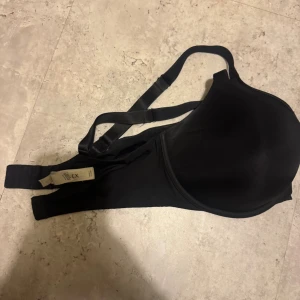 Svart BH Lilja 85E - Svart BH från Lindex, namn Lilja i storlek 85E.. BH:n har justerbara axelband och slät kupa för en clean look. Perfekt för dig som vill ha en basic och bekväm topp med enkel design. Ej push-up. Enbart använd någrs gånger