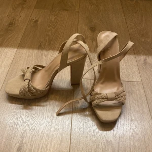 Beige mockasandaler med klack Anna Field - Snygga sandaler från Anna Field i beige mocka med flätad rem över tårna och smala remmar som går runt fotleden. Skorna har hög blockklack och öppen tå med en modern fyrkantig form. Perfekta för dig som vill ha en chic och trendig look.