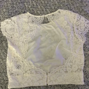 Vit spetsblus från Gina Tricot - Säljer en vit blus från Gina Tricot med blommigt spetsmönster och korta ärmar. Blusen har rund halsringning, knappar i ryggen och är fodrad framtill. Perfekt för dig som gillar romantisk och feminin stil.