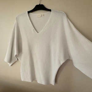 Vit stickad tröja med v-ringning Cyrus - Vit stickad tröja i storlek M. Tröjan är v-ringad och är tillverkad i ett mjukt stickat material med svagt våfflad struktur. Modellen är loose fit med breda, tre-kvartslånga ärmar. Så fin till både kjol och byxor. 80% bomull (rayon).