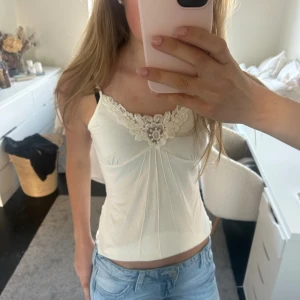 Vitt linne med spets detaljer - Köpt begagnad men inga defekter, jag har använt den en gång. Små pärlor på spetsen där framme och rosetter som man knyter över axlarna. På lappen står det strl 38 men skulle säga att den sitter som en s/xs.