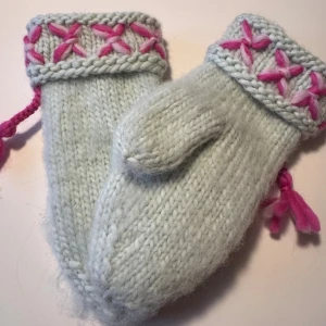 Handstickade ljusgrön vantar i lovikkastil  - Mysiga stickade vantar i ljusgrön ull med breda muddar dekorerade med handbroderade rosa och ljusrosa stjärnmönster. Vantarna har en klassisk tumme och snodd i rosa garn. Perfekta för kalla vinterdagar och riktigt gulliga detaljer. Damstorlek 