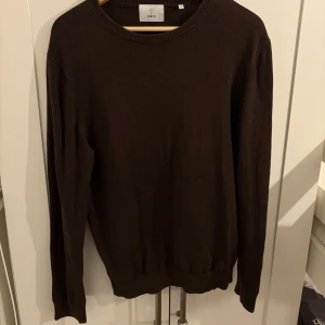 Mörkbrun stickad tröja från Bläck - En stilren mörkbrun stickad tröja från Bläck i storlek M. Tröjan har rund halsringning, ribbade muddar och är långärmad. Perfekt för lager-på-lager under kyliga dagar.