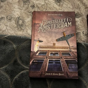 Gömstället i Amsterdam - Följ med på ett spännande tidsreseäventyr till 40-talets Amsterdam! Milton och Iona måste rädda sina vänner och möter Anne Frank under andra världskriget. Perfekt för unga som gillar historia, action och mysterier. Del två.  Har även del ett. Nästan som ny, bara läst en gång.