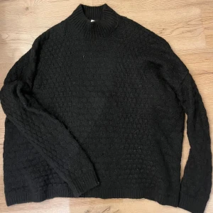 Svart stickad  - Svart stickad från H&M. Tröjan har en hög krage, långärmad design och ett snyggt strukturerat mönster över hela plagget. Perfekt för dig som gillar en enkel men cool look med lite extra textur. Oversized.
