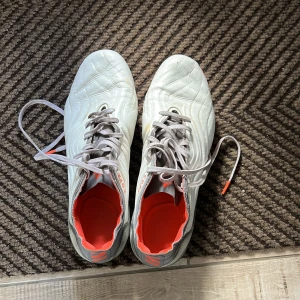 Adidas Copa Sense+ vita fotbollsskor - Säljer ett par Adidas Copa Sense+ fotbollsskor i vitt med grå och röda detaljer. Skorna har snörning, rund tå och platt sula med röda dobbar. Ovandelen är i syntetmaterial och insidan har en röd accent. Perfekta för dig som vill sticka ut på planen.