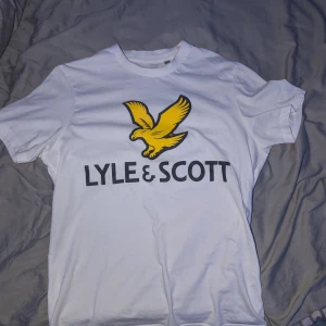 Vit Lyle & Scott t-shirt - Vit t-shirt från Lyle & Scott med stor gul fågel och svart logga på bröstet. Klassisk rund hals och korta ärmar. Skön bomullskvalitet som passar perfekt till jeans eller shorts. Enkel och stilren design med tydlig streetkänsla. Strl M skriv för frågor, bilder och offer 🤞🏼