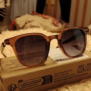 Bruna solglasögon med trädetaljer och sköldpaddsmönster - Helt nya solglasögon i box med brun transparent båge och mörka glas. Skalmarna har träliknande detaljer och små guldfärgade inslag vid gångjärnen. Rektangulär form som ger en cool vibe och passar perfekt till sommaren.