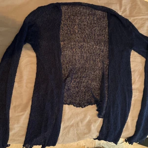 Mörkblå stickad kofta från Ulla Jacobsson - Säljer en tunn och lätt mörkblå stickad kofta från Ulla Jacobsson. Koftan har långärmad design och är öppen framtill utan knappar. Materialet är stickat och ger en luftig känsla, perfekt att slänga över en topp. Snygg att styla till jeans eller kjol.