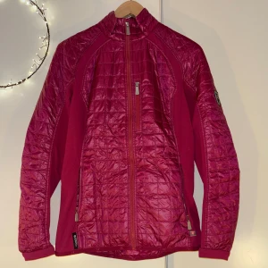 Rosa quiltad jacka från J.Lindeberg - Snygg rosa quiltad jacka från J.Lindeberg med dragkedja framtill och två fickor med dragkedja. Jackan har lång ärm, sportig look och badge på ena ärmen. Materialet är polyester och jackan har en lätt glansig finish.