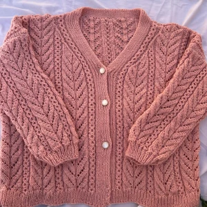 Rosa stickad kofta med pärlemorknappar - Superfin rosa stickad kofta med v-ringning och snyggt hålmönster. Koftan har tre pärlemorknappar framtill och ett litet diskret fickdetalj. Perfekt för lager-på-lager och ger en mysig vibe till din outfit.