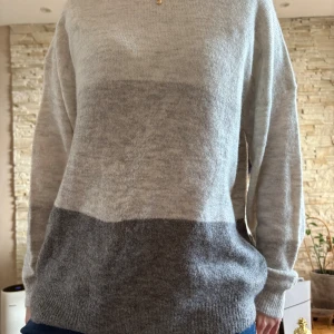 Gråmelerad stickad tröja Jacqueline de Yong - Mysig stickad tröja från Jacqueline de Yong i tre nyanser av grått. Tröjan har en avslappnad passform, rund halsringning och långa ärmar. Perfekt för lager-på-lager och chill dagar.