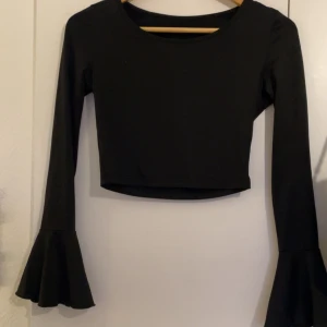 Svart croppad topp med trumpetärm - Svart långärmad croppad topp med snygga trumpetärmar. Enkel och stilren design med rund halsringning, perfekt för att lyfta din outfit med en cool detalj. Mjuk och stretchig känsla.