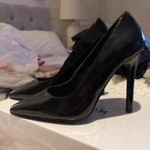 Svarta lackpumps från Nelly - Snygga svarta pumps i glansigt lackmaterial från Nelly. Skorna har spetsig tå och hög klack som ger en elegant och trendig look. Perfekta för dig som vill sticka ut med en klassisk men edgy stil.