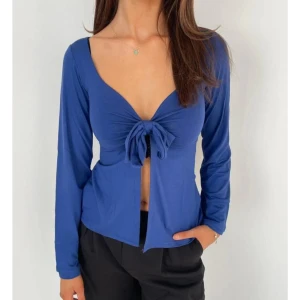 Design by si- Blå långärmad omlottopp med knyt - Snygg blå omlottopp med lång ärm och djup v-ringning. Toppen har ett knyt framtill som ger en cool och trendig look. Materialet är mjukt och stretchigt, perfekt för att skapa en avslappnad men ändå stilren outfit. Passar dig som gillar att sticka ut med detaljer. Xs/S från design by si