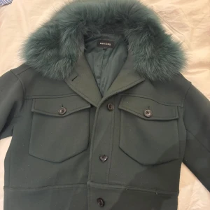 Mörkgrön pälsjacka från Meotine XS/S - Snygg mörkgrön pälsjacka från Meotine med fluffig krage i päls och stora fickor framtill. Perfekt för dig som vill sticka ut med en unik jacka i höst och vinter. Den har en knapp som är lite trasig som man kan se på sista bilden men de går fortfarande att knäppa annars är den jätte fräsch och inte använd så mycket.