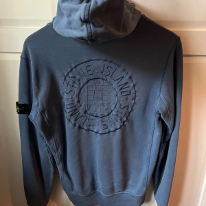 Ljusblå hoodie Stone Island  - Säljer en blå hoodie från Stone Island Junior med stor broderad logga på ryggen och klassisk patch på ärmen. Tröjan har huva, känguruficka och är tillverkad i mjuk bomull. Den är ungefär i storlek xs och i väldigt bra skick!