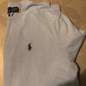Ralph lauren tröja i mycket fint skick - Snygg ljusblå stickad tröja från Ralph Lauren med klassisk broderad logga på bröstet. Tröjan har rund halsringning och är perfekt för dig som gillar stilrena och tidlösa plagg. Passar lika bra till jeans som till chinos.