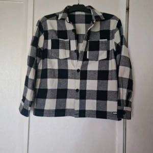 Svart och vitrutig skjorta  - Snygg rutig skjorta från Kappahl med klassisk krage och två bröstfickor. Skjortan har knappar framtill och är långärmad. Skjortan är väldigt sparsamt använd.